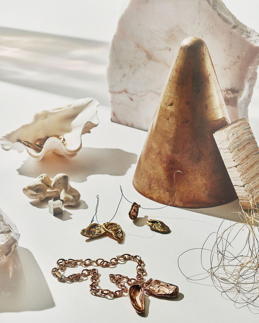 Still life shot of a copper necklace, shells, and geometric shapes in front of a white background, with shadows.