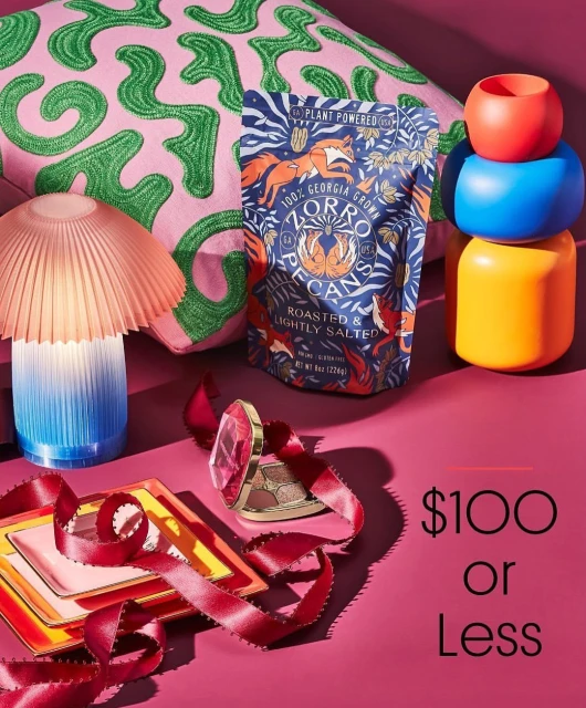 Still life of decorative objects including a throw pillow, lamp, colorful containers, and a bag of Zorro pecans against a pink background.