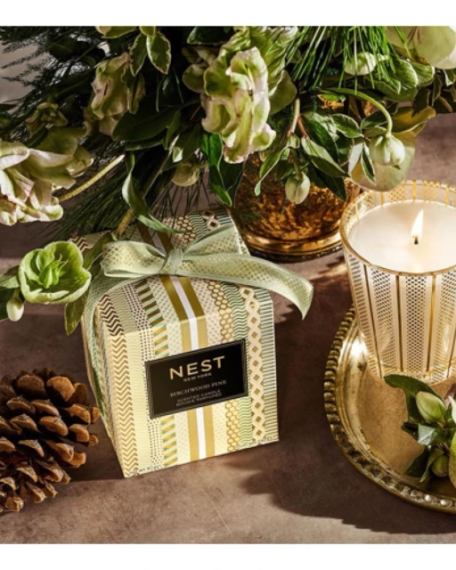 Elegant still life featuring a Nest Birchwood Pine candle, pinecone, and flower arrangement, set against a soft, neutral backdrop.