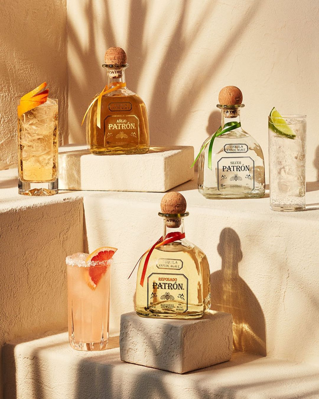 Four tequila bottles, two cocktails, and minimal props, arranged on blocks with a neutral background and diffused studio lighting.