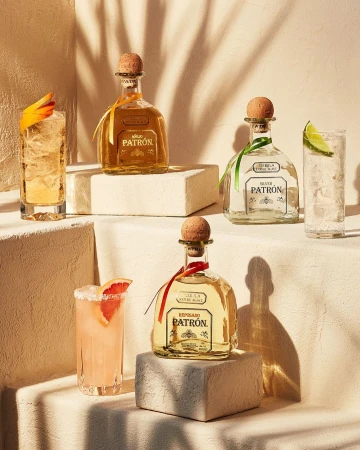 Four tequila bottles, two cocktails, and minimal props, arranged on blocks with a neutral background and diffused studio lighting.