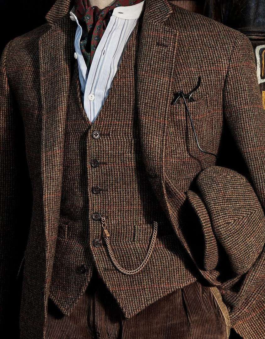 Close-up studio shot of a tweed suit with vest, flat cap, shirt and necktie, accessorized with a pocket watch and chain.