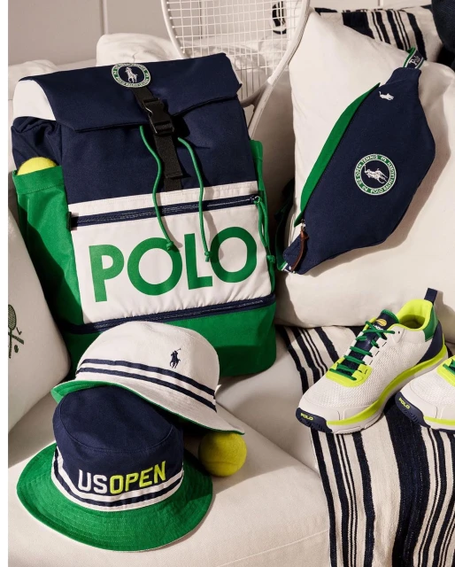 Polo Ralph Lauren tennis gear, including a backpack, belt bag, hat, tennis ball, and shoes on a striped white sofa, presents a sporty aesthetic.