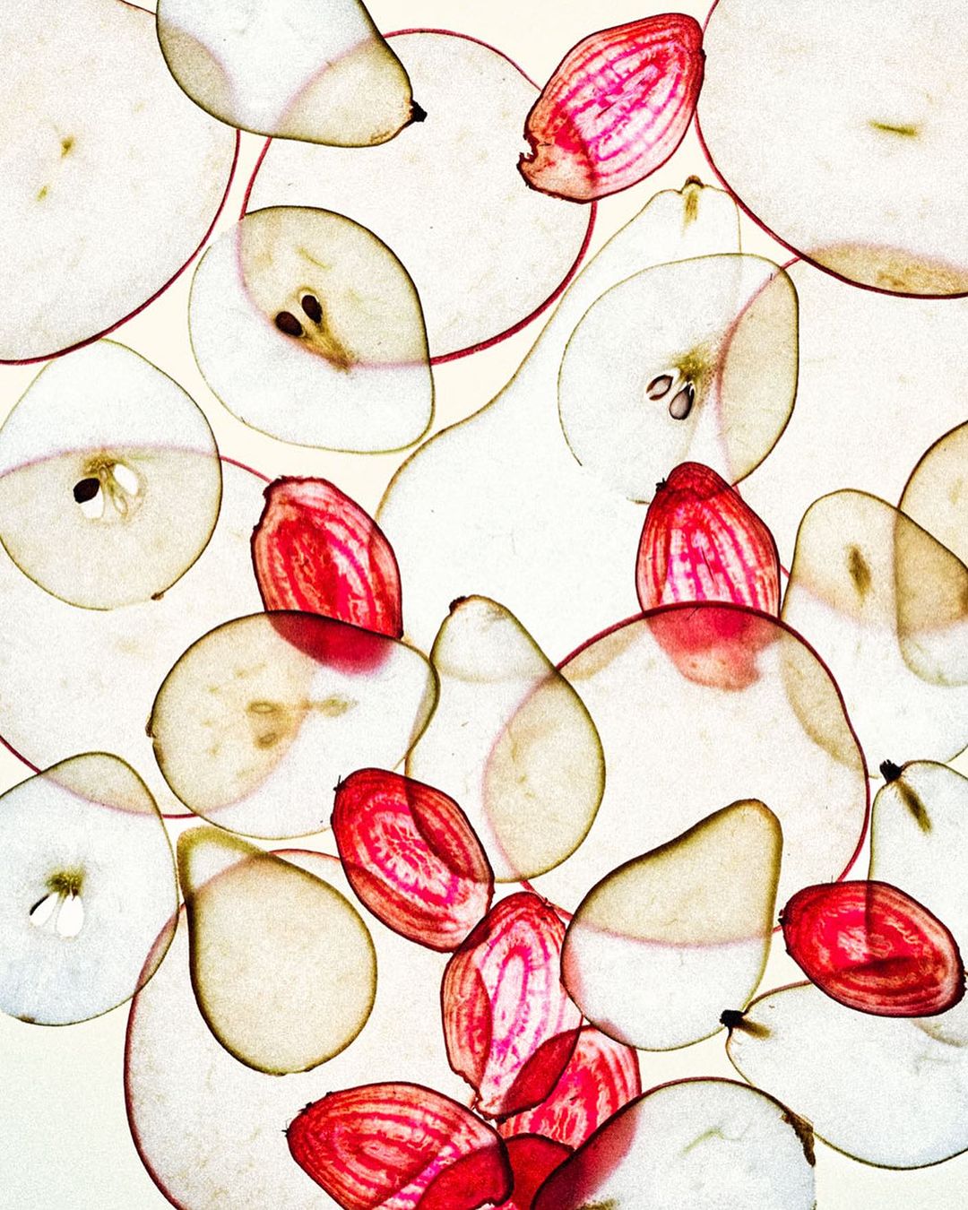 Overlapping slices of pears and beets create a vibrant food art composition on a bright background, showcasing their colors and textures.