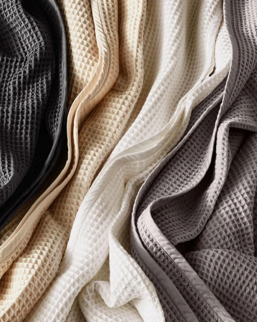 Arrangement of four textured waffle blankets in a high-angle shot, displaying a range of neutral colors from dark grey to beige to white.