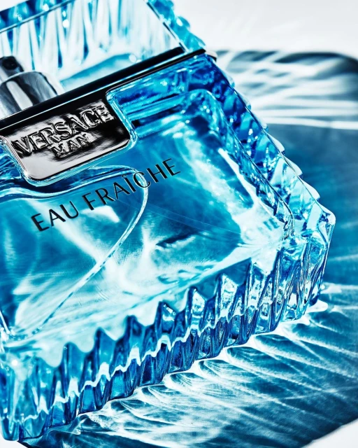 Close-up studio shot of Versace Man Eau Fraiche cologne bottle with a textured blue glass design and silver accents against a white background.