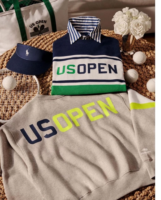 Still life of tennis-themed Ralph Lauren clothing and accessories, including shirts, sweater, tote bag, visor, tennis balls, and racket.