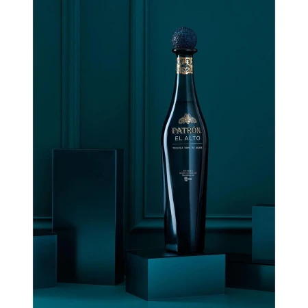 A bottle of Patron El Alto tequila is centered on dark blocks in a studio with a teal background, highlighting its premium presentation.