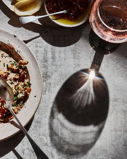 Overhead shot of table setting with a plate of food, bowl of cherries in syrup, glass of wine, and lemon wedges, showing culinary still life.