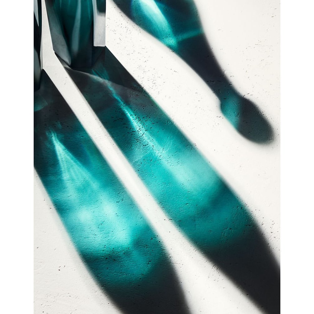 Abstract shot of teal light and shadow patterns cast on a textured white surface, creating an artistic and minimalist composition.