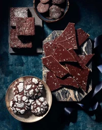 Overhead food photography of chocolate bark, brownies, and cookies arranged on a dark mottled surface by Kate Mathis.