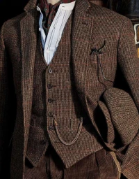 Close up of a man wearing a brown tweed three piece suit, striped shirt, patterned necktie, and holding a flat cap.