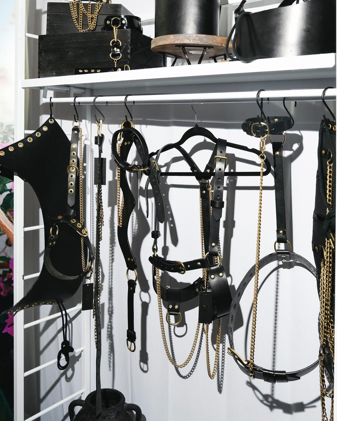 Display of black leather and gold chain harnesses and accessories hanging in an organized retail setting against a white background.