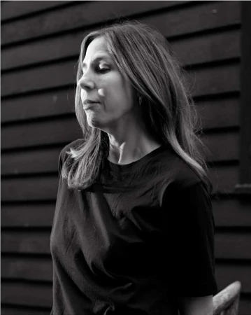 Portrait of a woman wearing a black t-shirt outdoors with dark wooden slat wall in the background