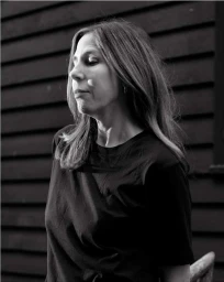 Portrait of a woman wearing a black t-shirt outdoors with dark wooden slat wall in the background