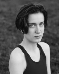 Close-up monochrome portrait of a woman with short dark hair wearing a dark tank top, looking directly at the camera