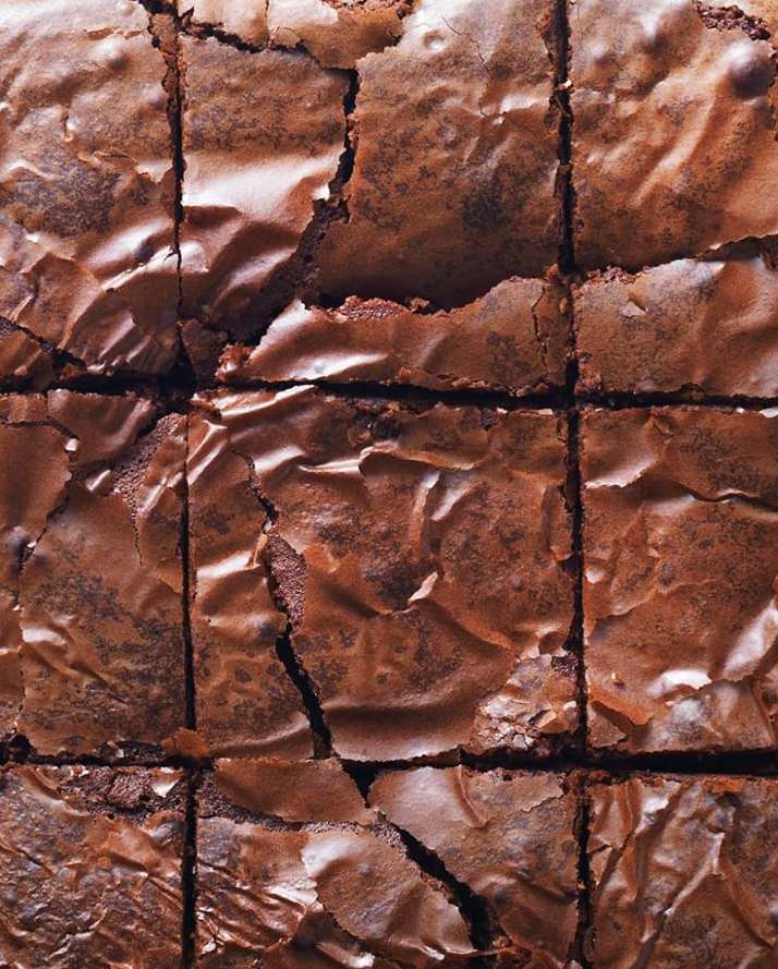 Close-up of a freshly baked batch of fudge brownies, cut into squares, showcasing a rich, dark chocolate color and slightly crinkled top.