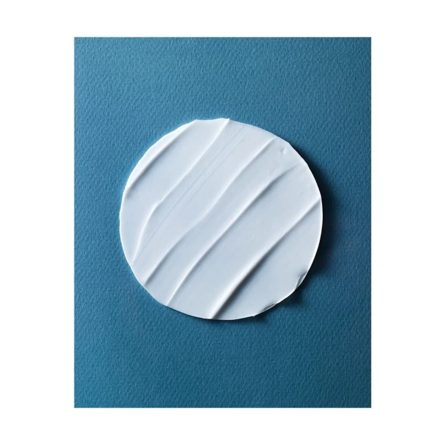 Close-up of a circular dollop of white cream with textured stripes on a textured blue background. Beauty shot for skincare.
