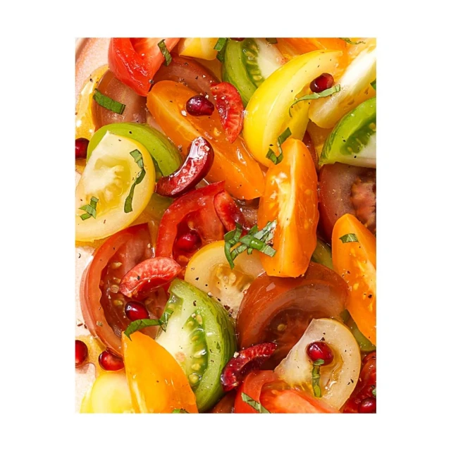 Overhead close-up of a vibrant tomato salad featuring an assortment of colorful tomatoes, herbs, and pomegranate seeds.