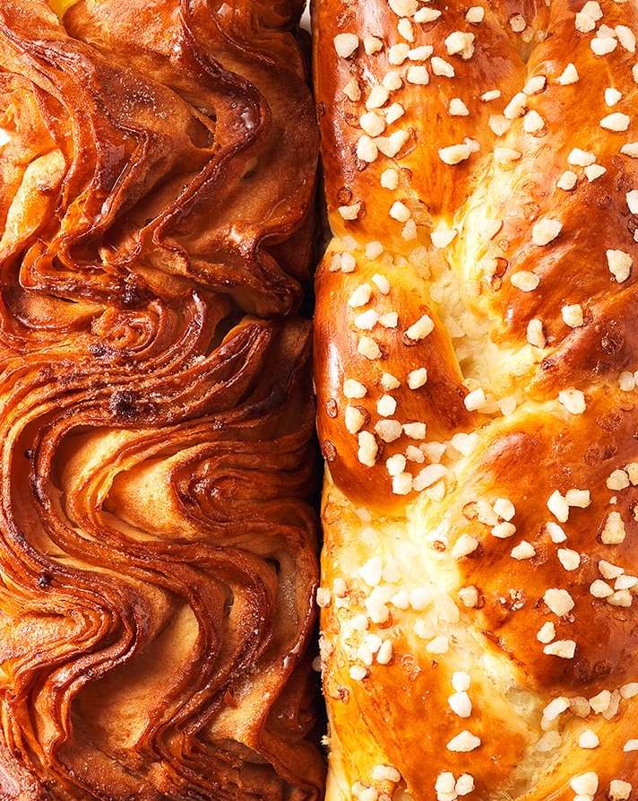 Close-up of braided breads with golden-brown crusts, one topped with white pearl sugar, showing intricate patterns of dough and baking details.