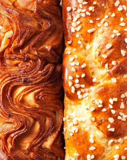 Close-up of braided breads with golden-brown crusts, one topped with white pearl sugar, showing intricate patterns of dough and baking details.