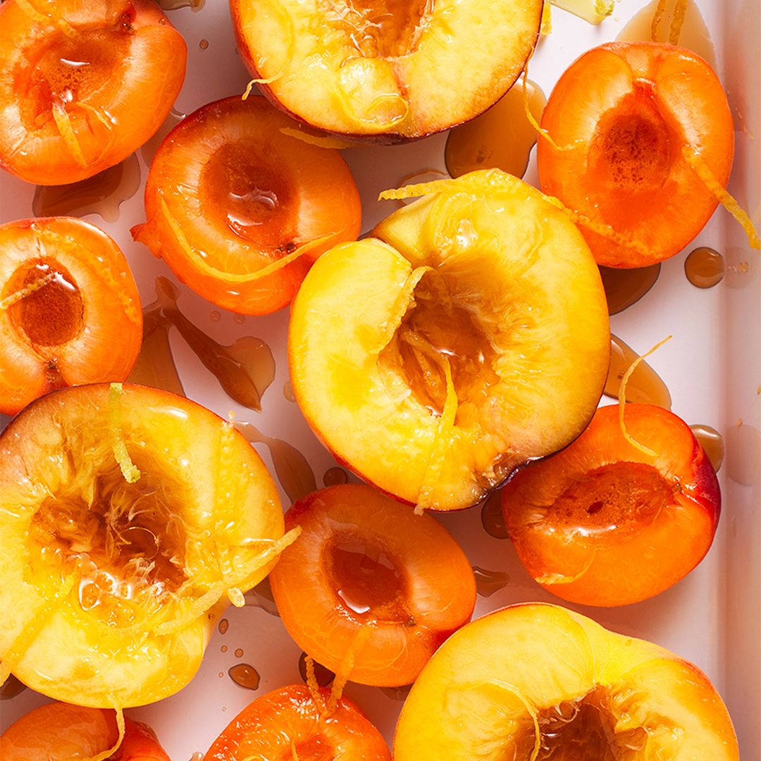 Overhead shot of sliced peaches with syrup and zest. Ripe peaches are halved and pitted, drizzled with syrup, and topped with lemon zest.