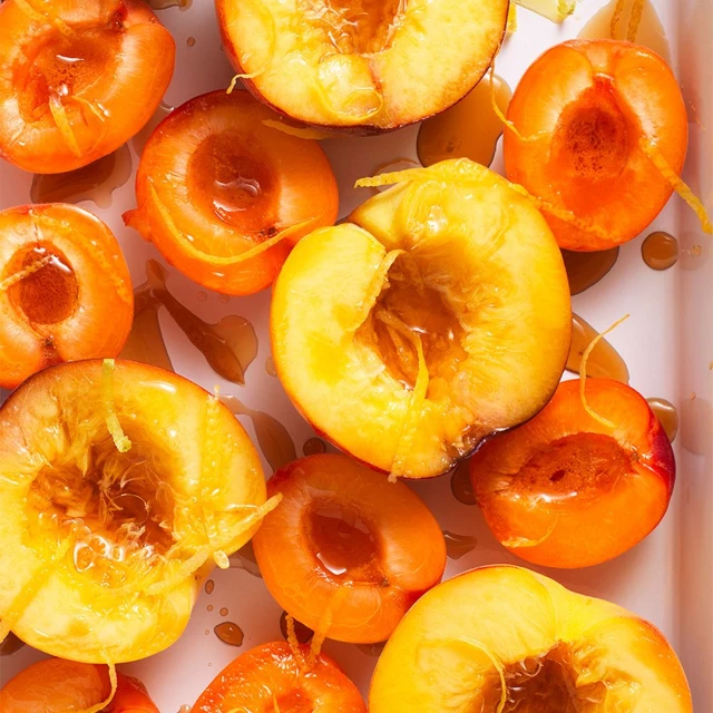 Overhead shot of sliced peaches with syrup and zest. Ripe peaches are halved and pitted, drizzled with syrup, and topped with lemon zest.