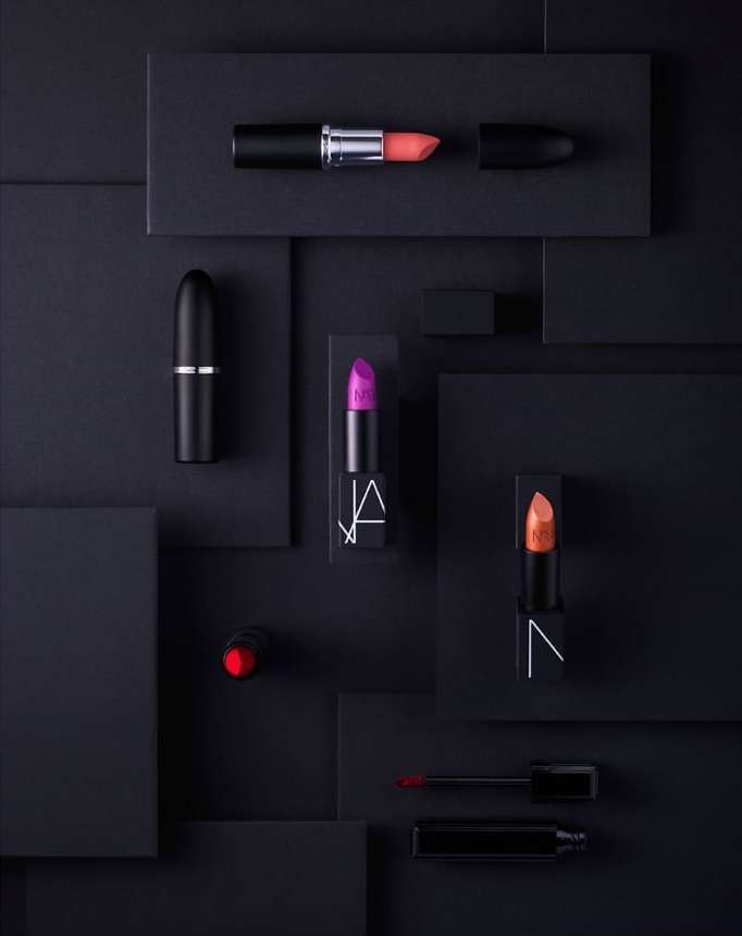 Elevated beauty product photography: several NARS brand lipsticks in a flat lay against a geometric black background.