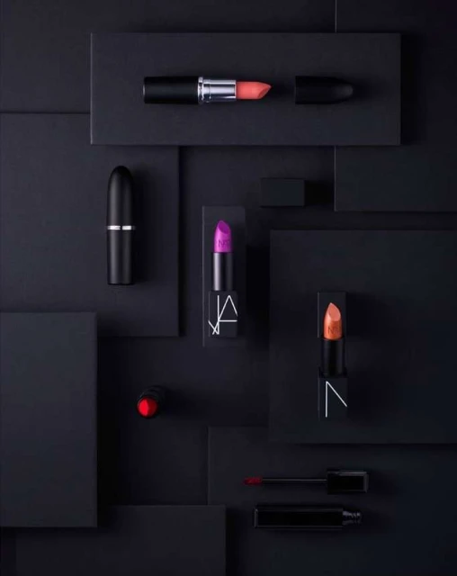 Elevated beauty product photography: several NARS brand lipsticks in a flat lay against a geometric black background.