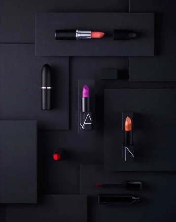 Elevated beauty product photography: several NARS brand lipsticks in a flat lay against a geometric black background.