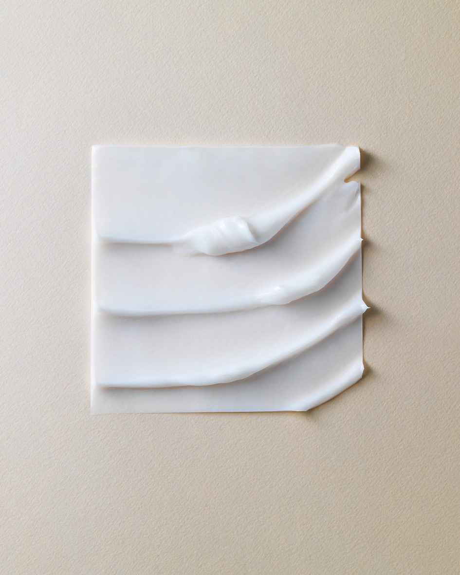 Close-up of white cosmetic cream or lotion spread on a square surface, set against a neutral beige background, product photography.