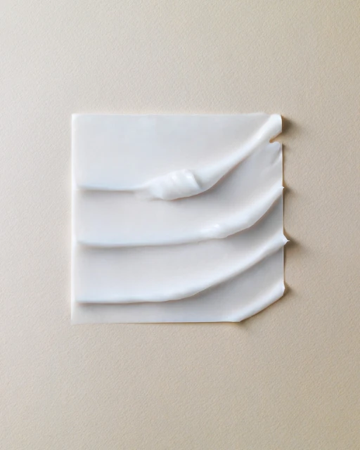 Close-up of white cosmetic cream or lotion spread on a square surface, set against a neutral beige background, product photography.