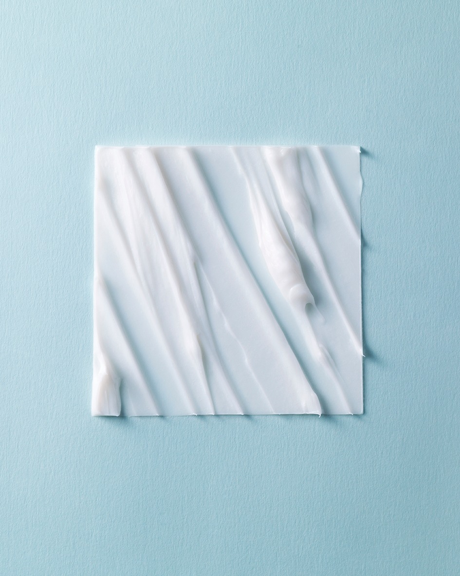 Close-up of thick white cream spread in an irregular pattern on a square surface against a pastel blue background, beauty concept.