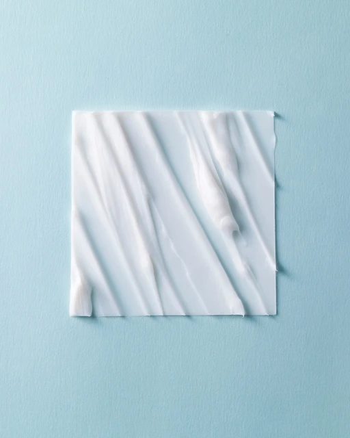 Close-up of thick white cream spread in an irregular pattern on a square surface against a pastel blue background, beauty concept.