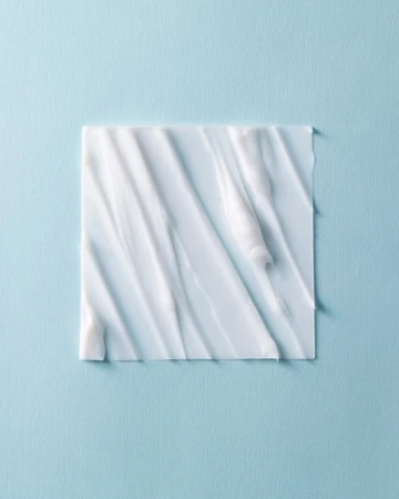 Close-up of thick white cream spread in an irregular pattern on a square surface against a pastel blue background, beauty concept.