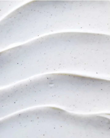 Close-up of a thick, white cosmetic cream with tiny dark granules, swirled to create a textured, wave-like surface pattern.