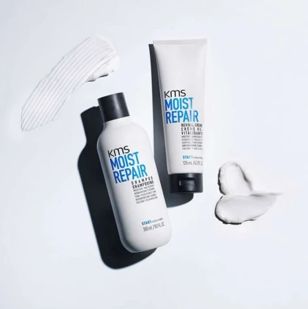 Two white bottles of KMS Moist Repair shampoo and revival creme are staged with white cream smears against a white background.