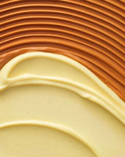 Abstract food photography of smooth, rippled pale-yellow and brown cream texture with curved lines and patterns for food-related design.