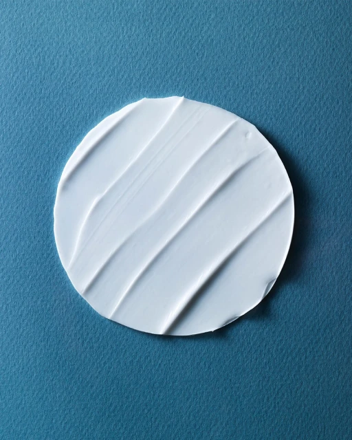 Close-up of a circular swatch of white cream or lotion with textured lines, set against a solid light blue background.