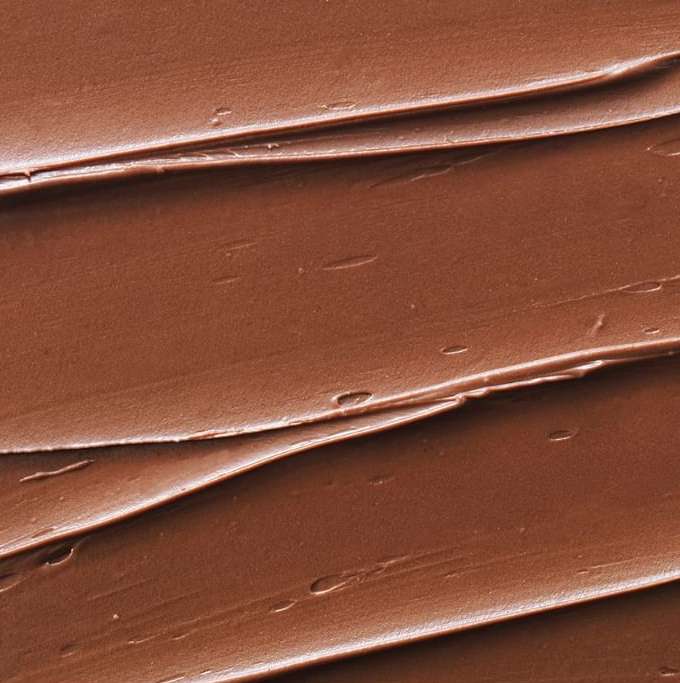 Close-up texture of a thick, brown spread with a rippled pattern; the food industry and creamy textures for culinary designs.