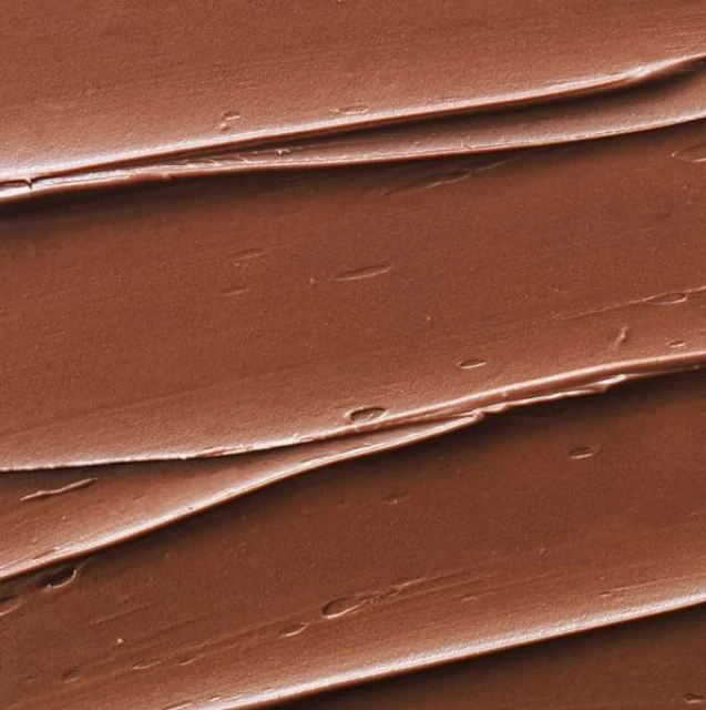Close-up texture of a thick, brown spread with a rippled pattern; the food industry and creamy textures for culinary designs.