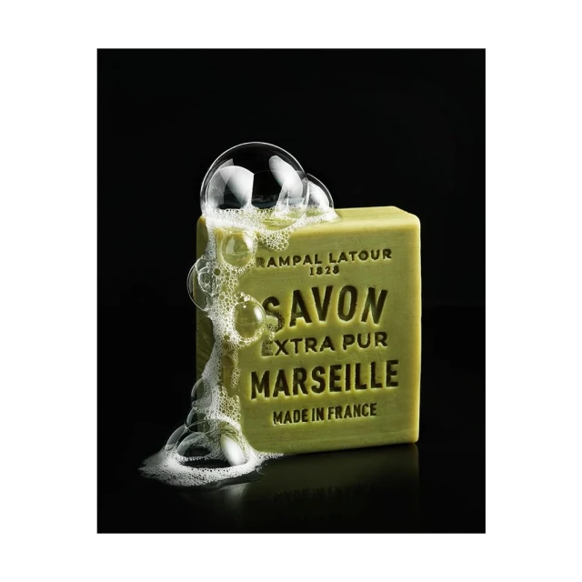 Olive-green bar of Savon Marseille Extra Pur soap with bubbles, shot in a product photography style on a black background.