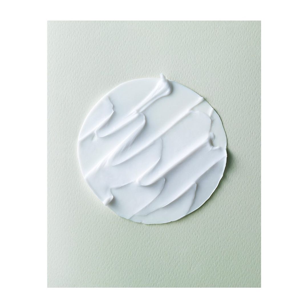 Close-up of white cream with thick, swirled texture on a light green background. Beauty product shot. Minimalist aesthetic.