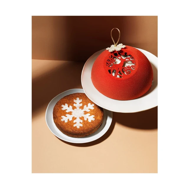 Overhead shot of round Christmas cakes on white plates against a two-tone tan background; holiday dessert concept.