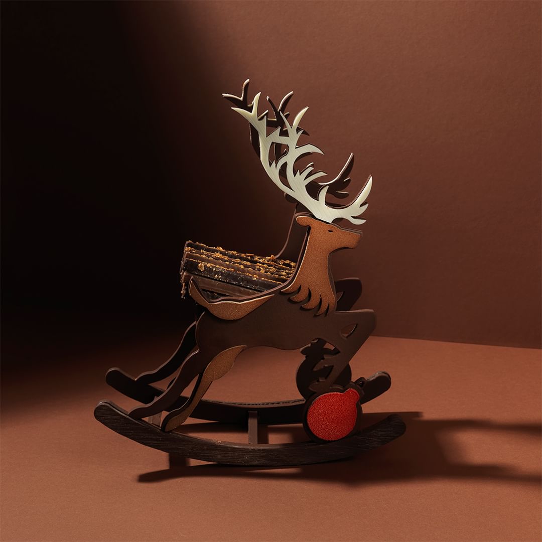 Whimsical wooden rocking horse deer Christmas decoration with festive red ornament against a warm brown background, soft lighting.