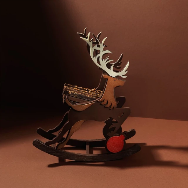 Whimsical wooden rocking horse deer Christmas decoration with festive red ornament against a warm brown background, soft lighting.