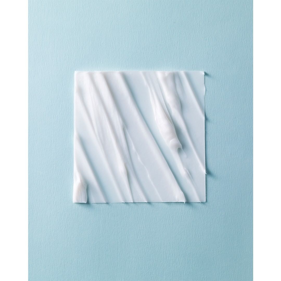 A square of white cream with textured swirls and patterns, centered on a light blue background, creating a minimalistic beauty product shot.