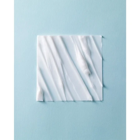 A square of white cream with textured swirls and patterns, centered on a light blue background, creating a minimalistic beauty product shot.