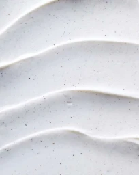 Close-up of smooth white cosmetic cream with small dark exfoliating particles in swirled ridges by Katell Bouniol