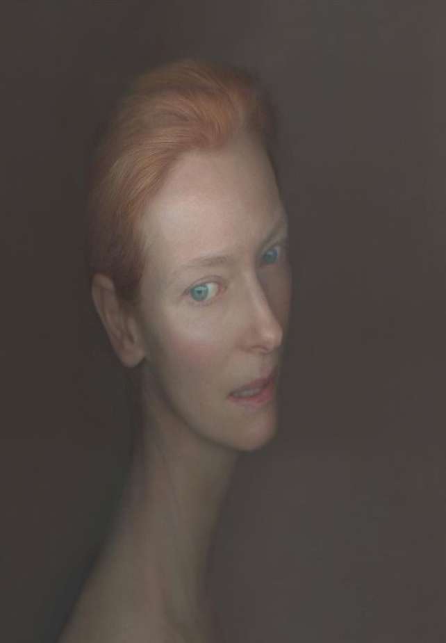 Headshot of an adult female with short red hair and light skin, set against a dark background in a portrait style.